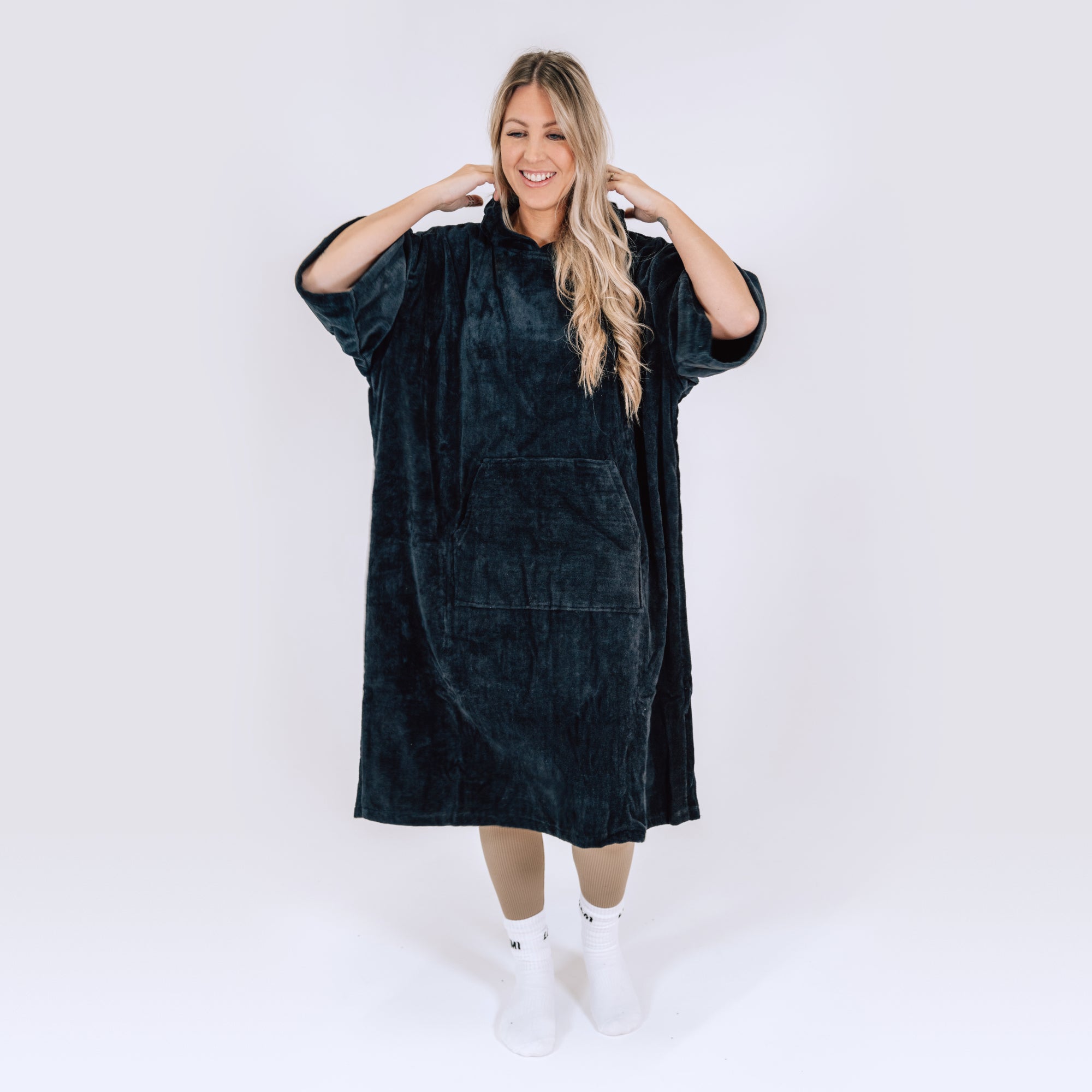 LUMI Towel Poncho shown as an oversized hooded robe in luxurious black cotton fabric, featuring roomy design with front pocket, modeled against white background, displaying full-length coverage and comfortable fit