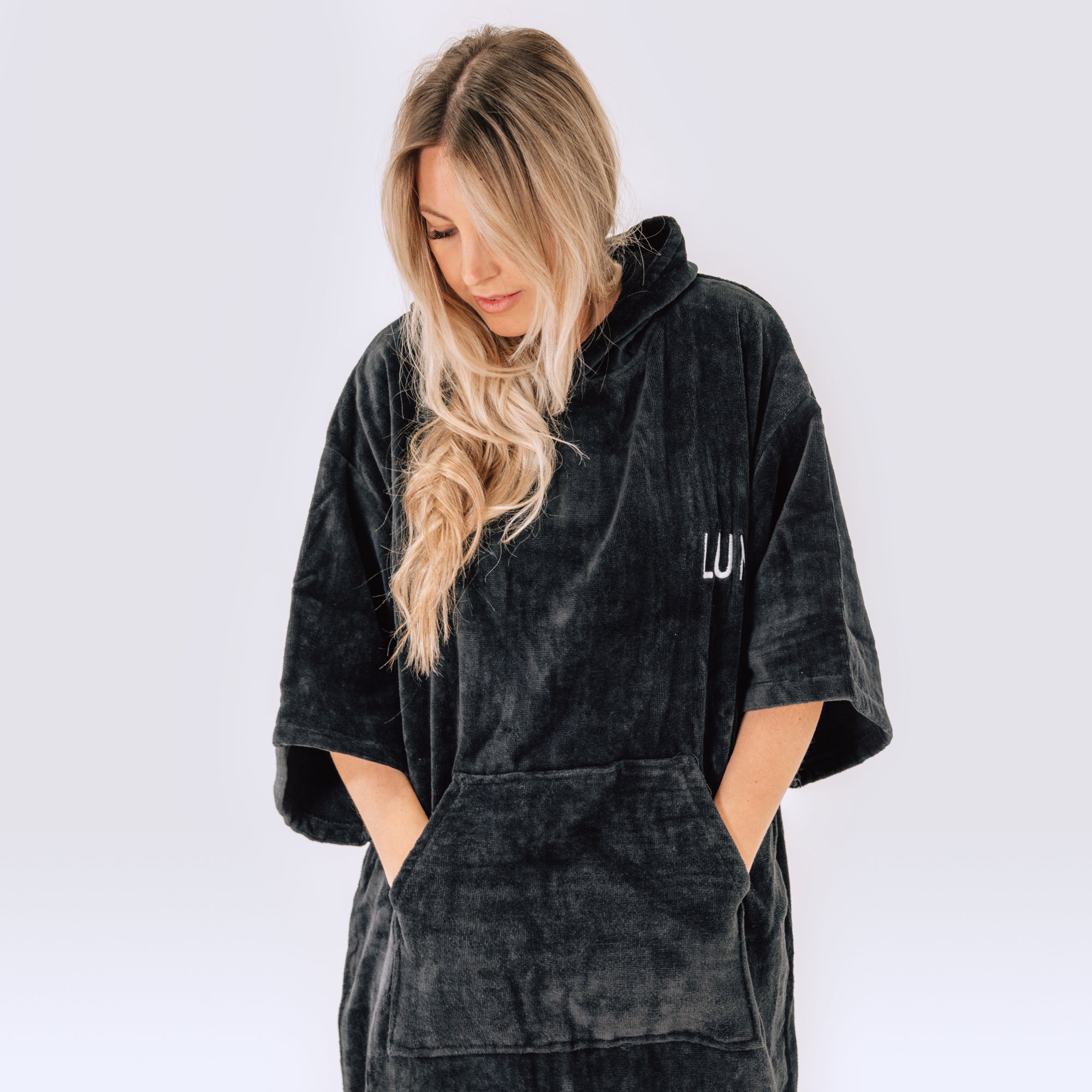 LUMI Towel Poncho in plush black cotton shown on a model, featuring oversized hooded design with front pocket, wide sleeves, and cozy fabric texture, ideal for post-swim or ice bath coverage