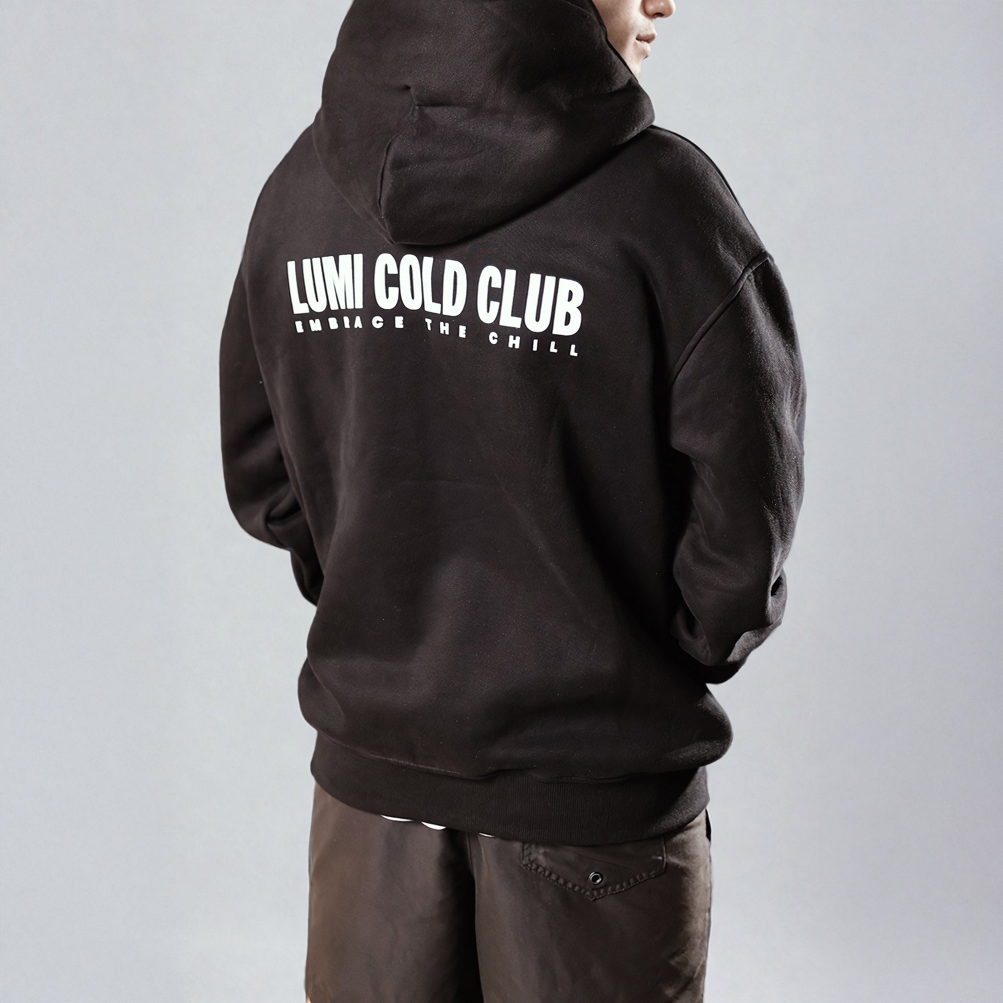 Back view of Unisex LCC Oversized Hoodie Black featuring white 'LUMI COLD CLUB' text graphic print, showing relaxed fit and dropped shoulders against light background.