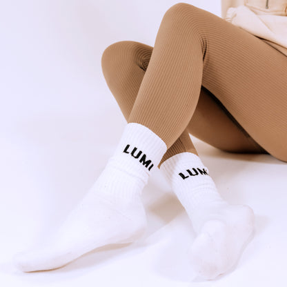 Pro Bamboo Socks (4 Pack) - White athletic socks with LUMI logo worn with brown leggings against white background, displaying elastic cuff and ribbed texture design, showcasing comfortable fit and sporty aesthetic