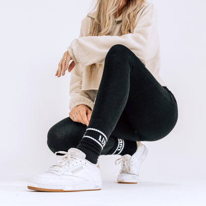 Pro Bamboo Socks with Stripes (4 Pack) shown on a model wearing black pants and white sneakers, displaying the LUMI branded sock design with contrasting stripe detail. Close-up lifestyle product shot against white background showcasing the athletic sock style and fit.